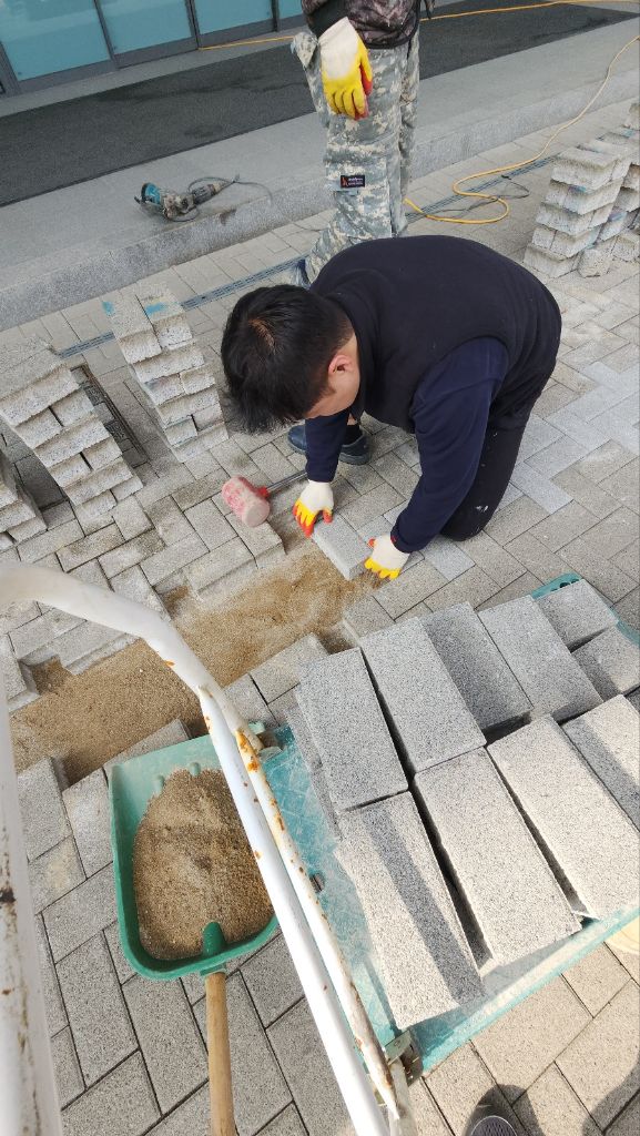 모래 기초 위에 회색 보도블럭을 한 장씩 맞춰 시공하는 작업자